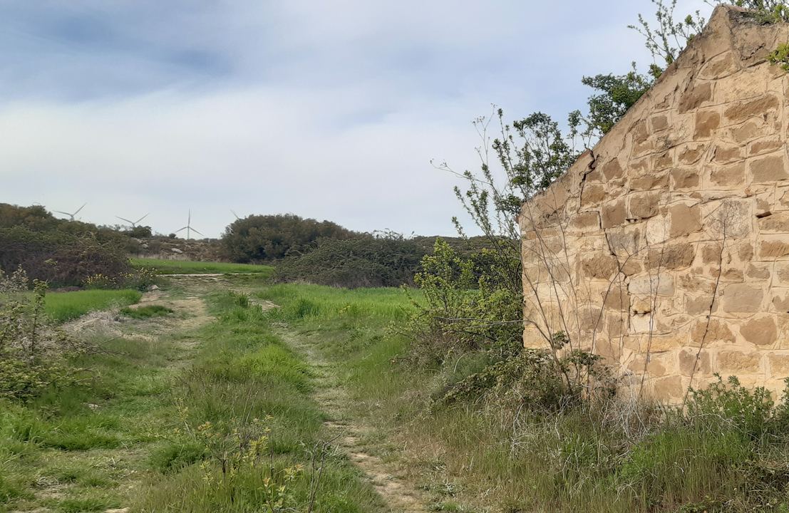 camino con molinos al fondo y pared de una casa a la derecha